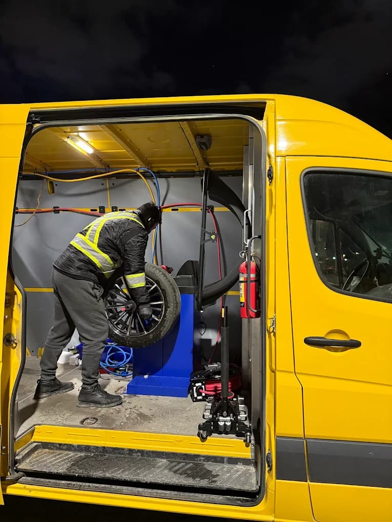 A GoldenNorth technician in a hi-vis vest balancing a wheel beside the yellow service van