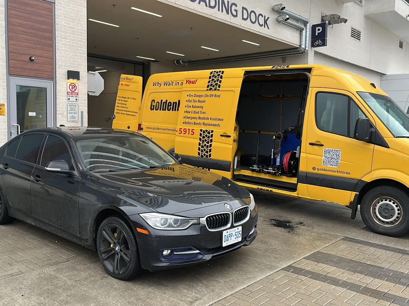 GoldenNorth technician servicing a gray BMW beside the yellow van at a loading dock